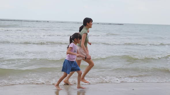 Asian family on vacation. Beautiful mother carry baby girl and run with big sister on beach together