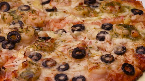Fried Pizza already Sliced with Seafood and Black Olives in the Overview on the Table.