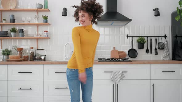 Happy Hispanic Curly Woman Listening to Music and Dancing at Home in the Kitchen