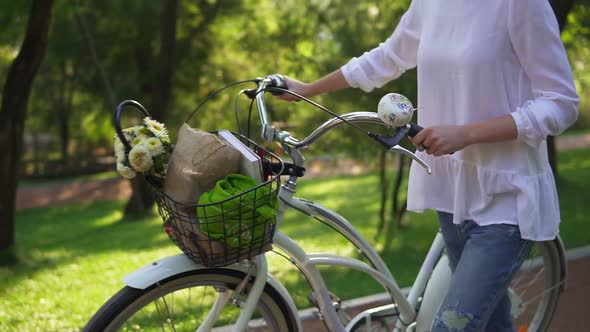 Closeup View of Woman's Hands Holding a Handlebar of a City Bicycle with a Basket with Flowers and