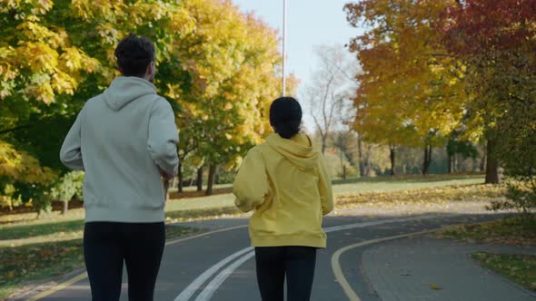 Man and Woman Running on a Track at the City Park in Sunny Autumn Morning