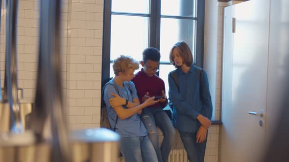 Happy Diverse Teenage Children Sitting on Sill in School Lavatory and Play on Smartphone