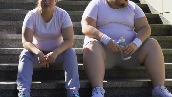 Chubby Man and Woman Resting After Hard Workout on Stairs, Breathing Heavily