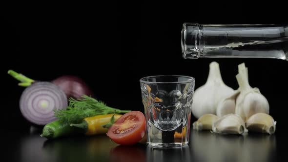 Pour Alcohol Drink Vodka From a Bottle in Shot Glass. Background with Vegetables