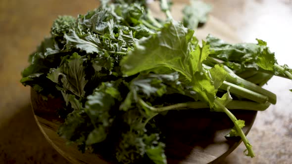 Clusters of stalks of fresh rapini on a round cutting board rotating in beautiful backlit light. Sha