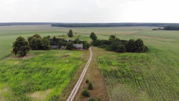 Aerial View of a Country Road and a Wooden House with Buildings Among the Trees on a Summer Day