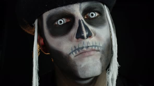 Scary Man with Carnival Makeup of Halloween Skeleton Opening His Eyes Against Black Background