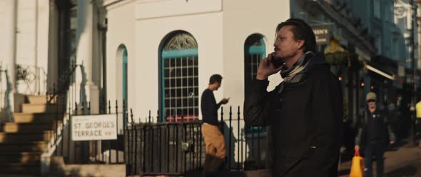 Man talking by his cellphone and greeting a friend coming out of a phone booth