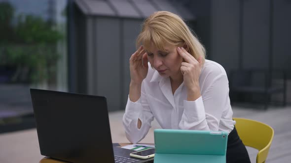 Overwhelmed Beautiful Woman Rubbing Temples Sitting with Laptop on Office Terrace
