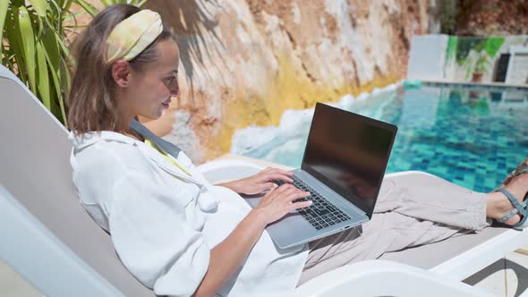 Camera Moving Behind and Around Happy Woman Enjoying Relaxing By the Pool with Laptop Computer with