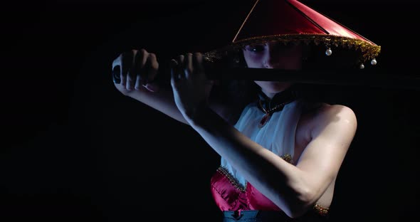 Gorgeous Young Woman with Asian Makeup and a Hat Holding a Katana