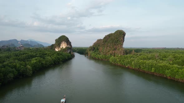 aerial drone flying backwards revealing a Thai longtail boat on a river between a two large green li