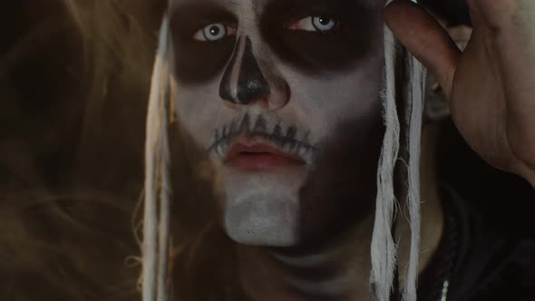 Close-up of Sinister Man with Skull Makeup Making Faces and Exhaling Cigarette Smoke From His Mouth