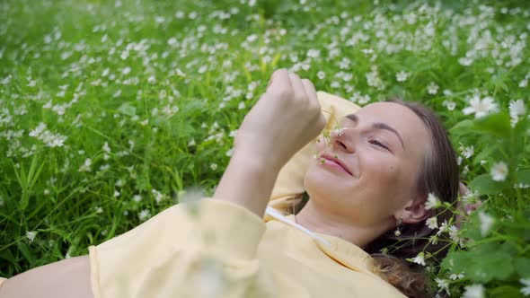 A Young, Healthy and Beautiful Girl Is Lying in the Grass and Sniffing Flowers