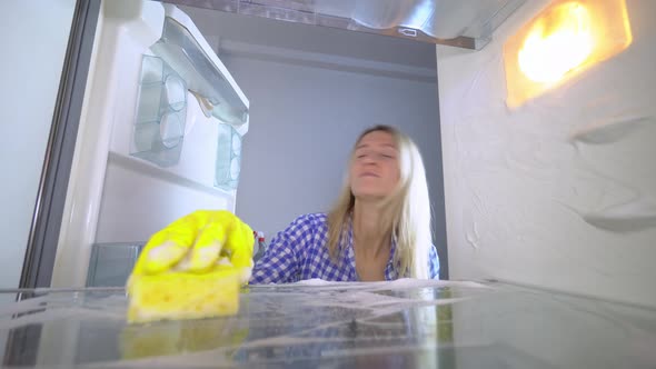 A disgruntled and irritated woman washes and cleans inside the refrigerator