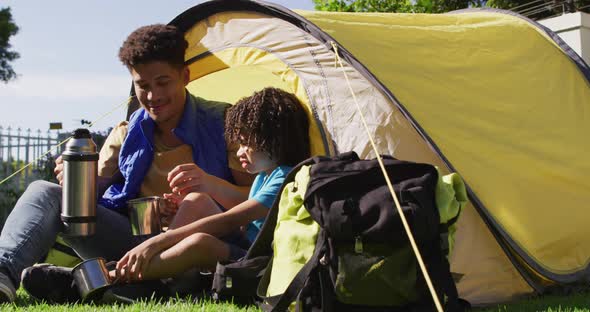 Happy biracial man and his son drinking from thermos flask in garden