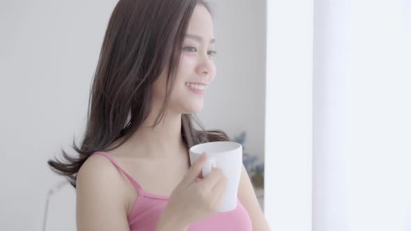 Beautiful young asian woman smile and drink a cup of coffee with relax in the morning at window.