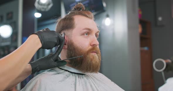 Closeup Face of Young Bearded Man Who is Sitting on the Barber's Chair Facing the Mirror and Female