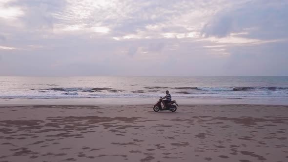 Drone view of a motorcycle going fast on the beach at sunset