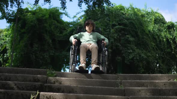 Front View Portrait Sad Disabled Boy in Wheelchair at Stairs with Summer Park at Background