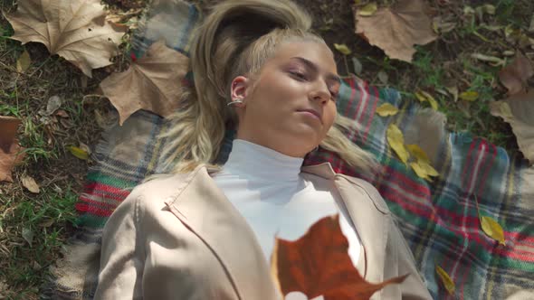 Smiling female lying on plaid with dry leaf in park