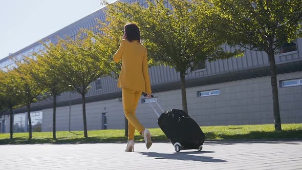 Attractive young business woman in a formal Suit pulls a Suitcase