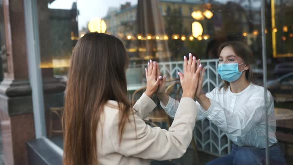 Two Women in Protective Masks Opposite Each Other Window Between Them