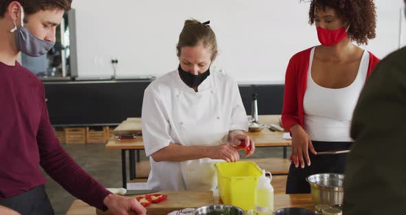 Caucasian female chef teaching diverse group wearing face masks