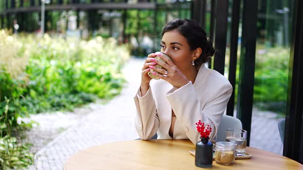 Young Business Woman Holding and Drinking Coffee in Street Cafe in City