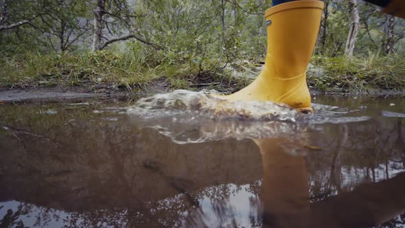 Crop person in yellow gumboots walking in puddle
