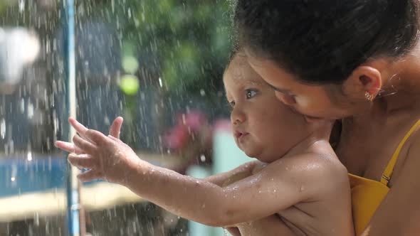 A Young Mother with a Child the Child is Up to a Year Old is Happy to Touch the Flow of Water