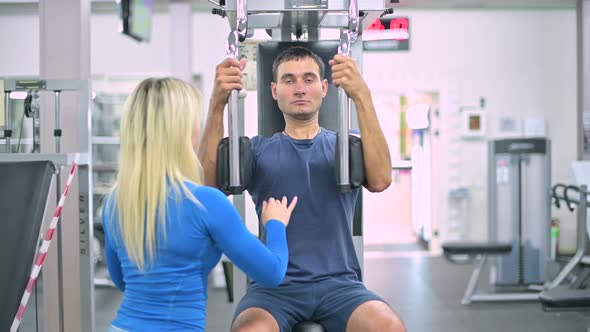 skinny guy does an exercise on an machine under the supervision of a trainer