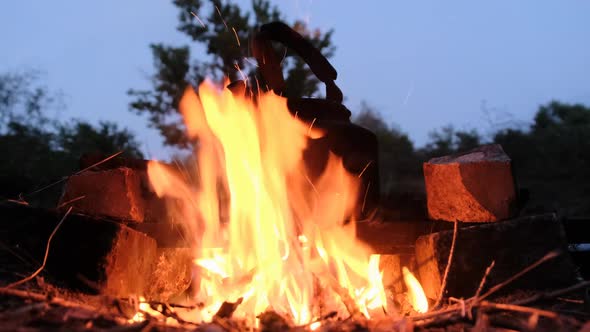 Old Tourist Kettle Standing on Campfire with Flames in Tourist Camp at Twilight