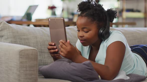 Happy african american girl lying on sofa using tablet