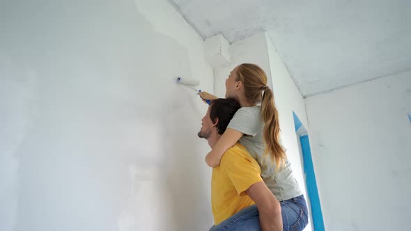 A Happy Man and Woman Paint the Wall Using a Roller Painter