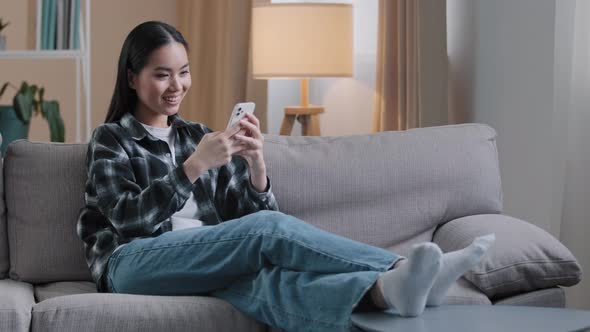 Asian Girl Woman Sitting on Sofa at Home Relaxing Watching News Feed on Social Media Choosing
