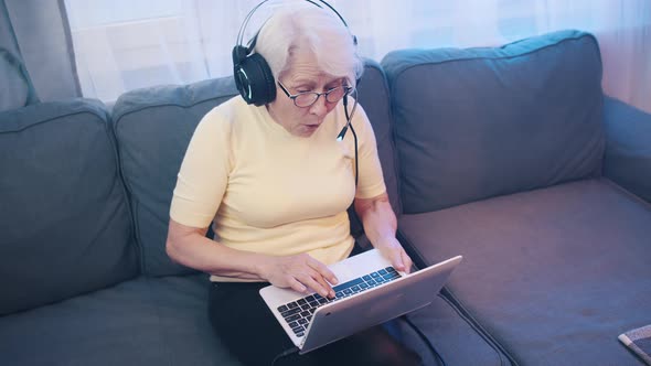 Elderly Woman with Headset Playing Video Games on the Laptop