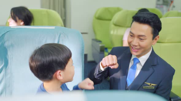 Asian professional flight attendant male walking on aisle and talking with little boy on airplane.