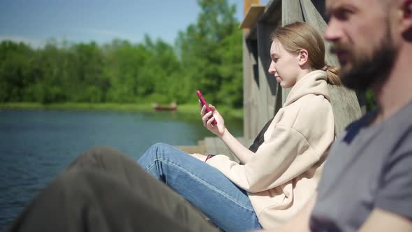 Woman Relaxes By the Lake with Phone and Man