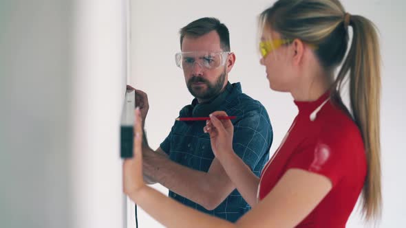 Joyful Couple Checks Wall Using Instrument in Spacious Room