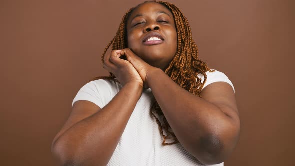 Grateful Black Woman Clasping Hands and Smiling Touched By Complement Brown Studio Background