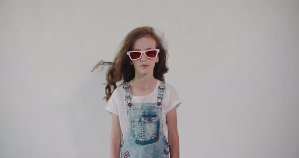 Portrait of a girl in denim overalls and sunglasses on a white background.	