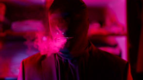 a Man in a Black Knitted Mask Without Eyes Lets Out a Stream of Smoke From Mouth in a Neon Flashing
