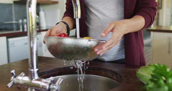 Midsection of caucasian pregnant woman washing vegetables in kitchen