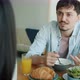 Happy Young Man Eating Breakfast and Talking to Woman Sitting at Table in Kitchen - VideoHive Item for Sale
