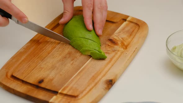 Closeup of woman hands with knife cutting avocado for salad on a wooden board