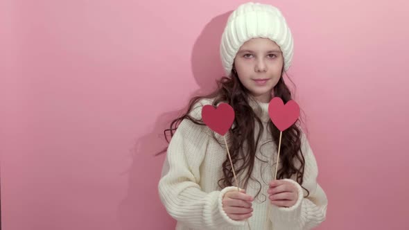 Happy Young Girl Wearing White Knitted Sweater Holding Red Hearts Over Eyes