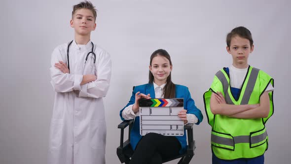 Positive Confident Little Producer Sitting on Chair with Clapping Board As Friends in Doctor and