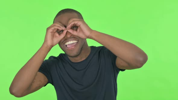 Searching Young African Man with Binocular Gesture on Green Background