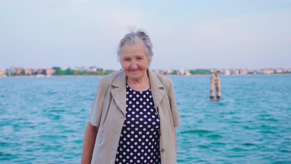 Elderly Woman Looks Into Camera Smiling Standing at Lagoon